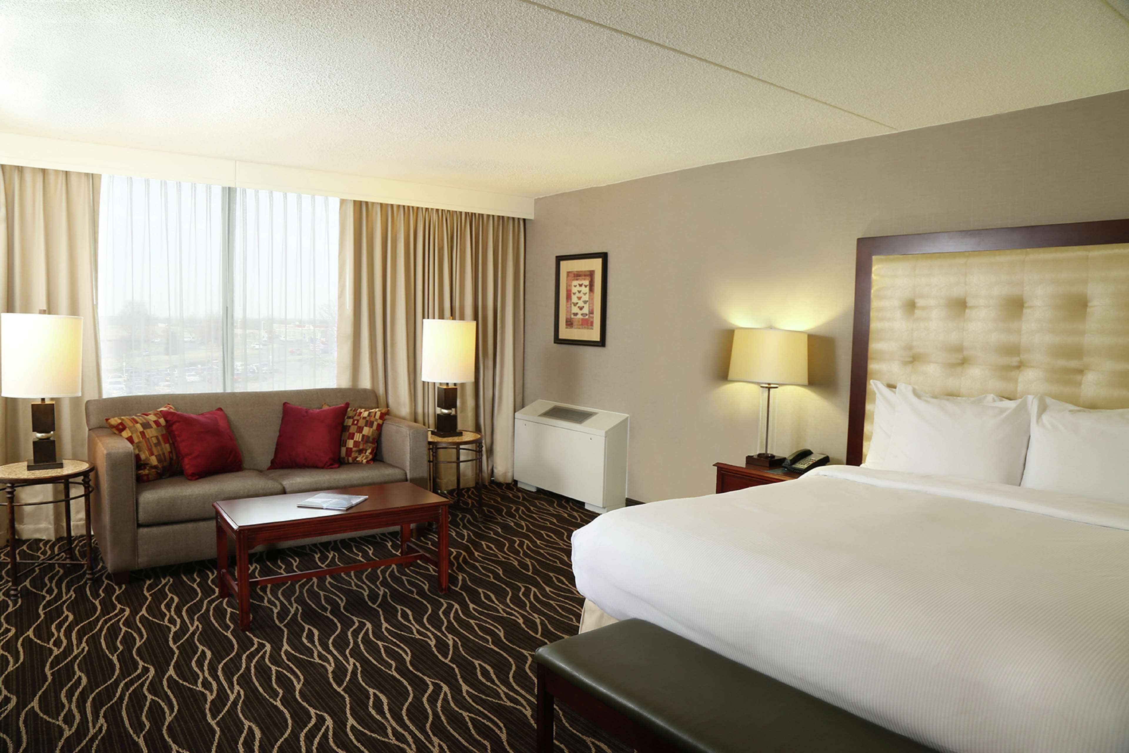 A hotel room with a bed, a sofa, a coffee table, two lamps, a telephone, and a picture on the wall.