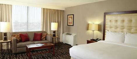 A hotel room with a bed, a sofa, a coffee table, two lamps, a telephone, and a picture on the wall.