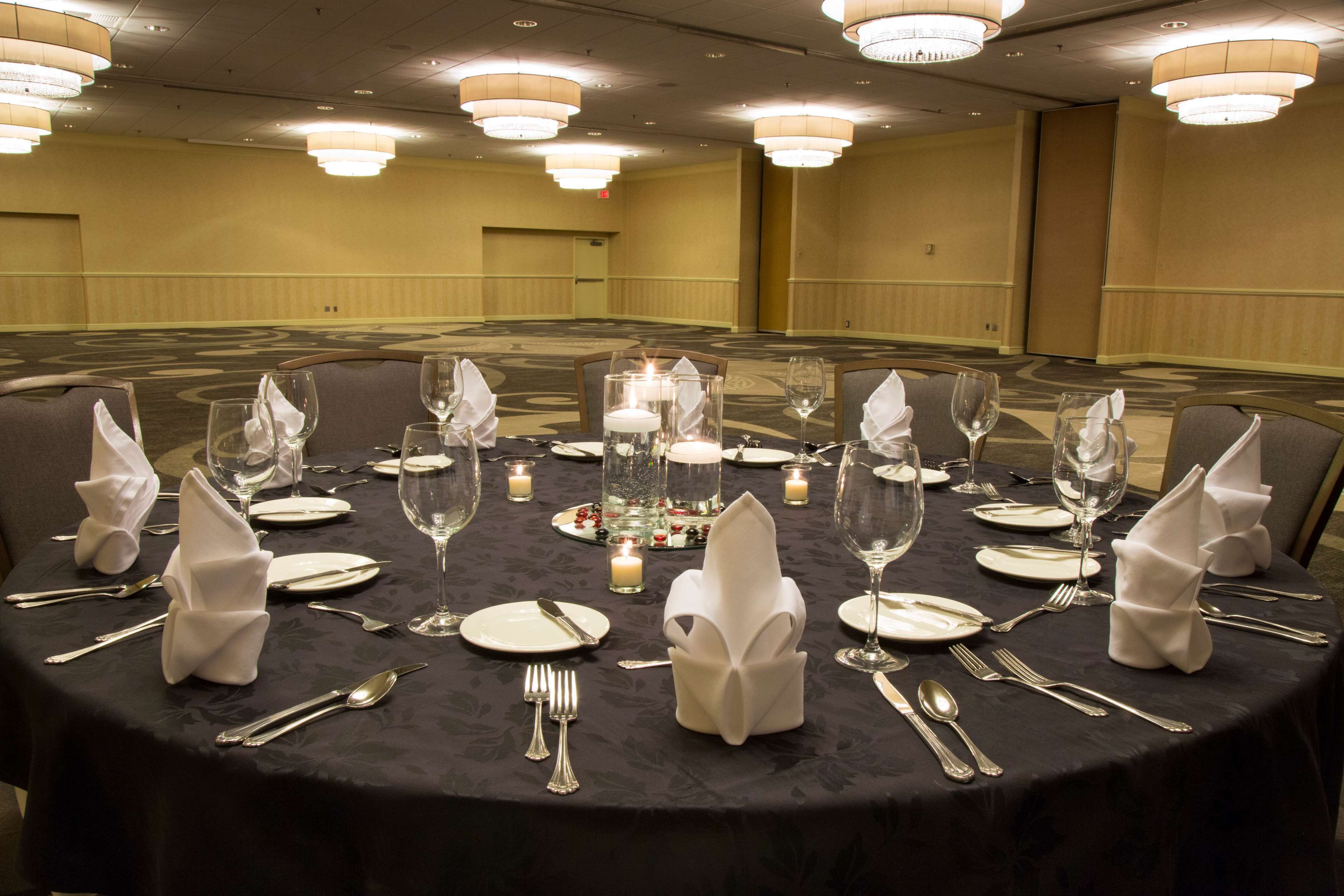 Una mesa redonda dispuesta para una cena formal, con velas, copas y servilletas dobladas.