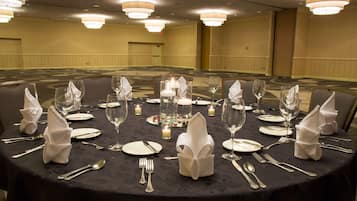 Una mesa redonda dispuesta para una cena formal, con velas, copas y servilletas dobladas.