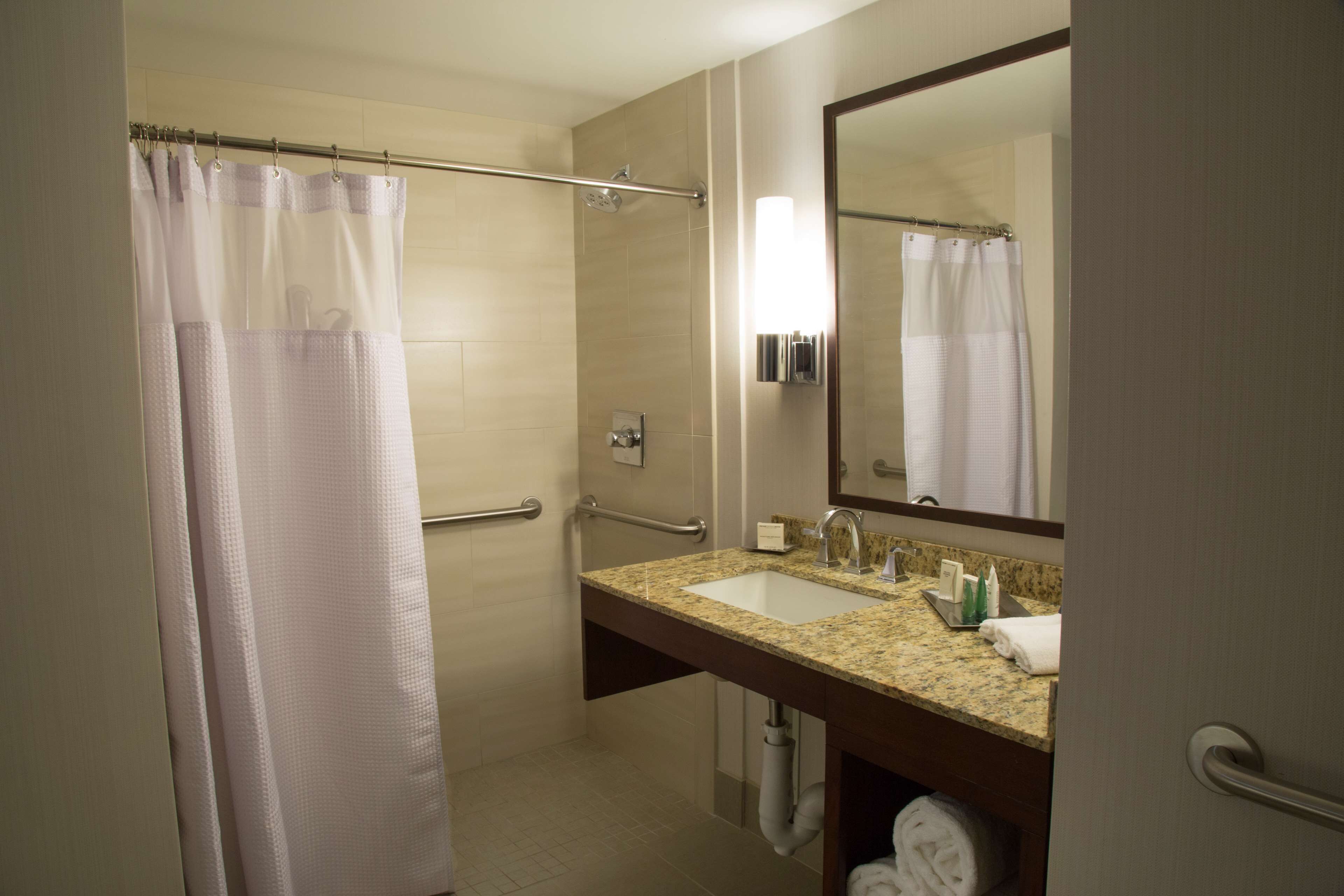 Un baño con ducha, lavabo, espejo y toallero.