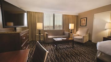 Een hotelkamer met een grote flatscreen televisie, twee fauteuils, een bank, een salontafel en een kamerbreed tapijt met dessin.