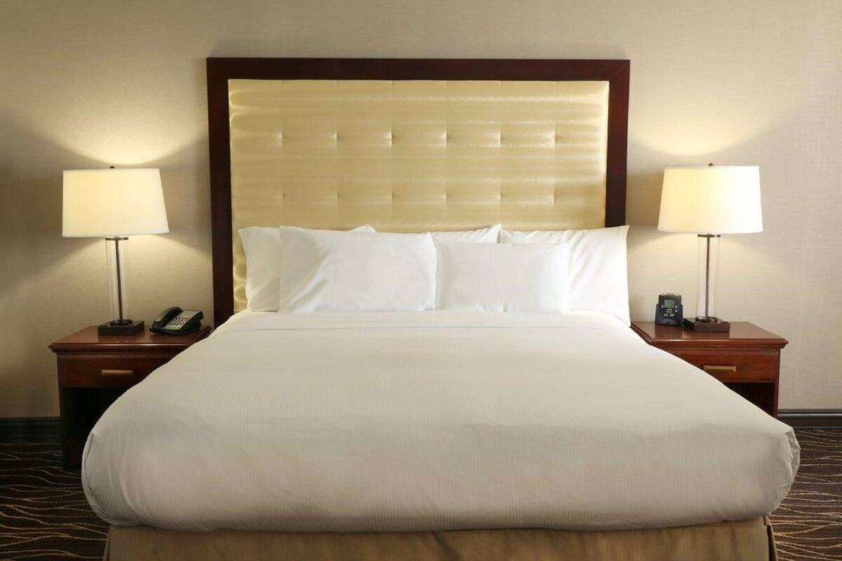Habitación de hotel con una cama grande, dos mesitas de noche con lámparas y un teléfono en cada mesita.