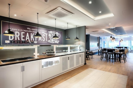 A modern breakfast bar with a large sign, pendant lighting, and a seating area with tables and chairs.. Premier Inn Köln City Centre