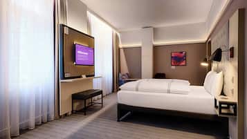 A hotel room with a bed, a TV, a desk, and a chair.