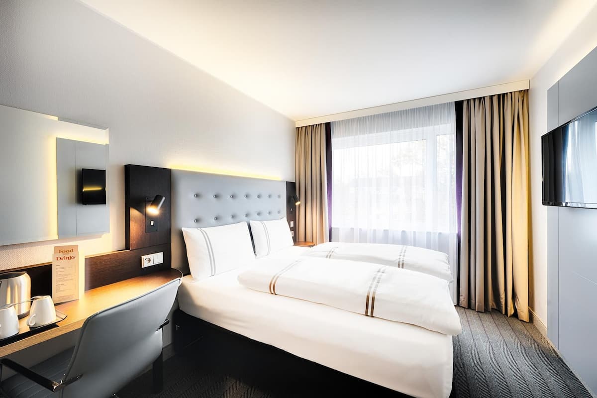 Une chambre d’hôtel équipée d’un lit, d’un bureau, d’une chaise, d’un téléviseur à écran plat et d’une fenêtre avec des rideaux.