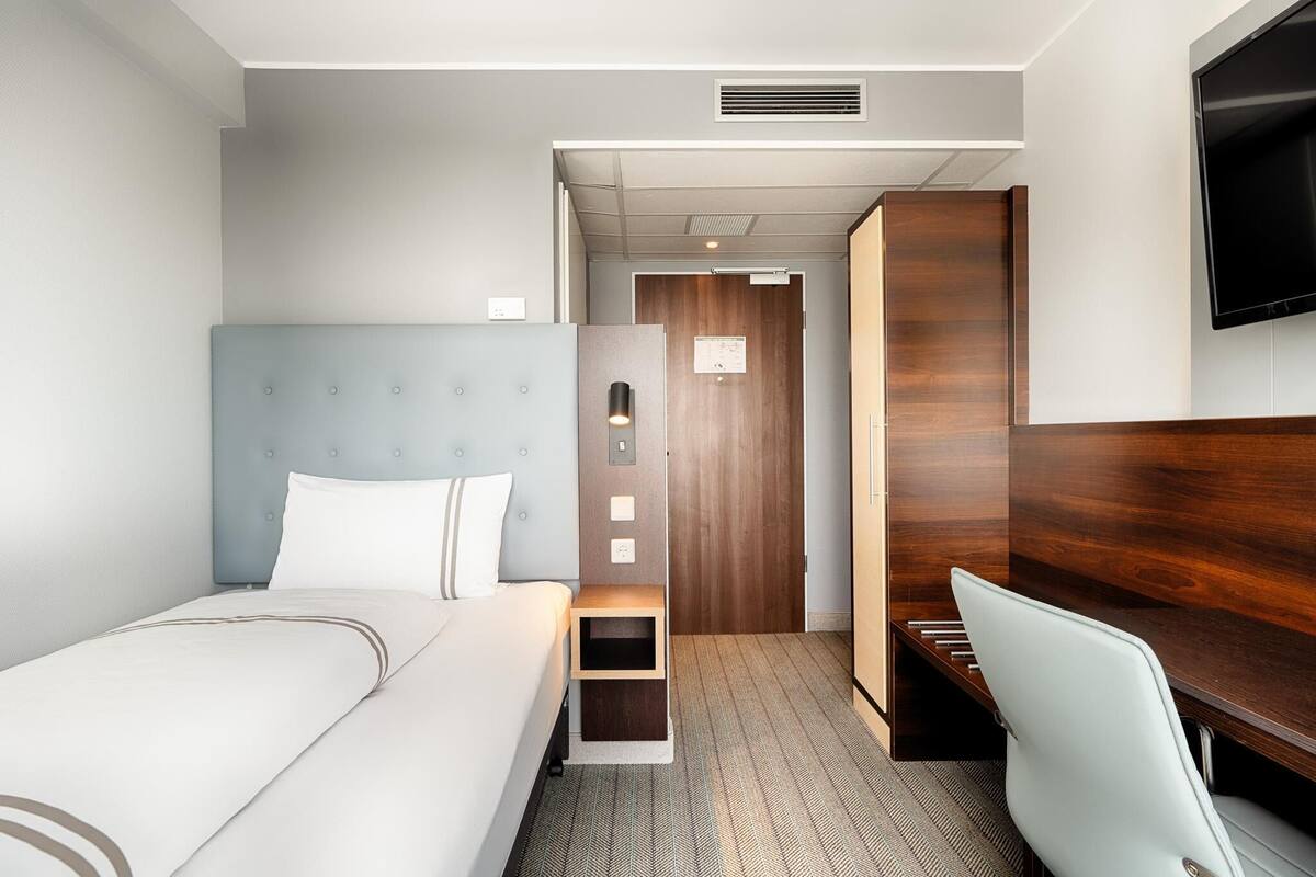 Une chambre d’hôtel comprenant un lit, un bureau, une chaise, une télévision et une armoire en bois.