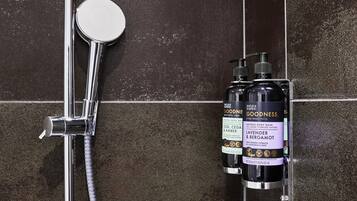 A shower with a chrome faucet and hose, and two bottles of Goodness Lavender & Bergamot body wash.