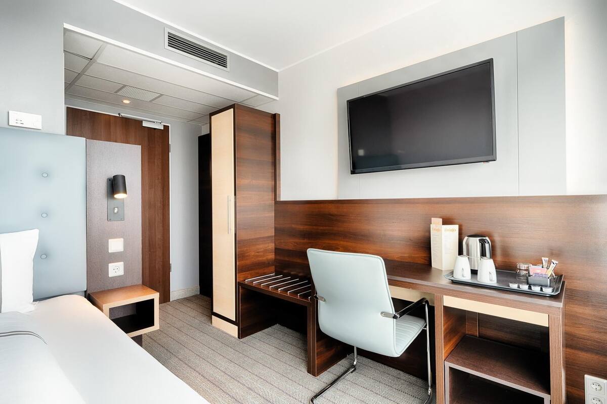 Une chambre d’hôtel comprenant un lit, un bureau avec une chaise, un téléviseur à écran plat, une machine à café et un plateau avec des tasses et une bouteille.