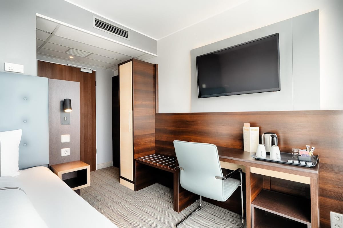 Habitación de hotel con cama, escritorio con silla, televisor de pantalla plana, cafetera y bandeja con tazas y una botella.