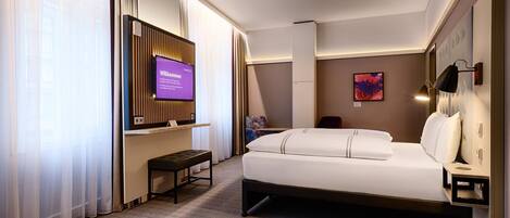 Una habitación de hotel con una cama, un televisor fijado a la pared, una mesita y un banco.