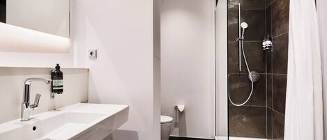 Un baño moderno con ducha envuelta en vidrio, un lavamanos blanco y un inodoro.