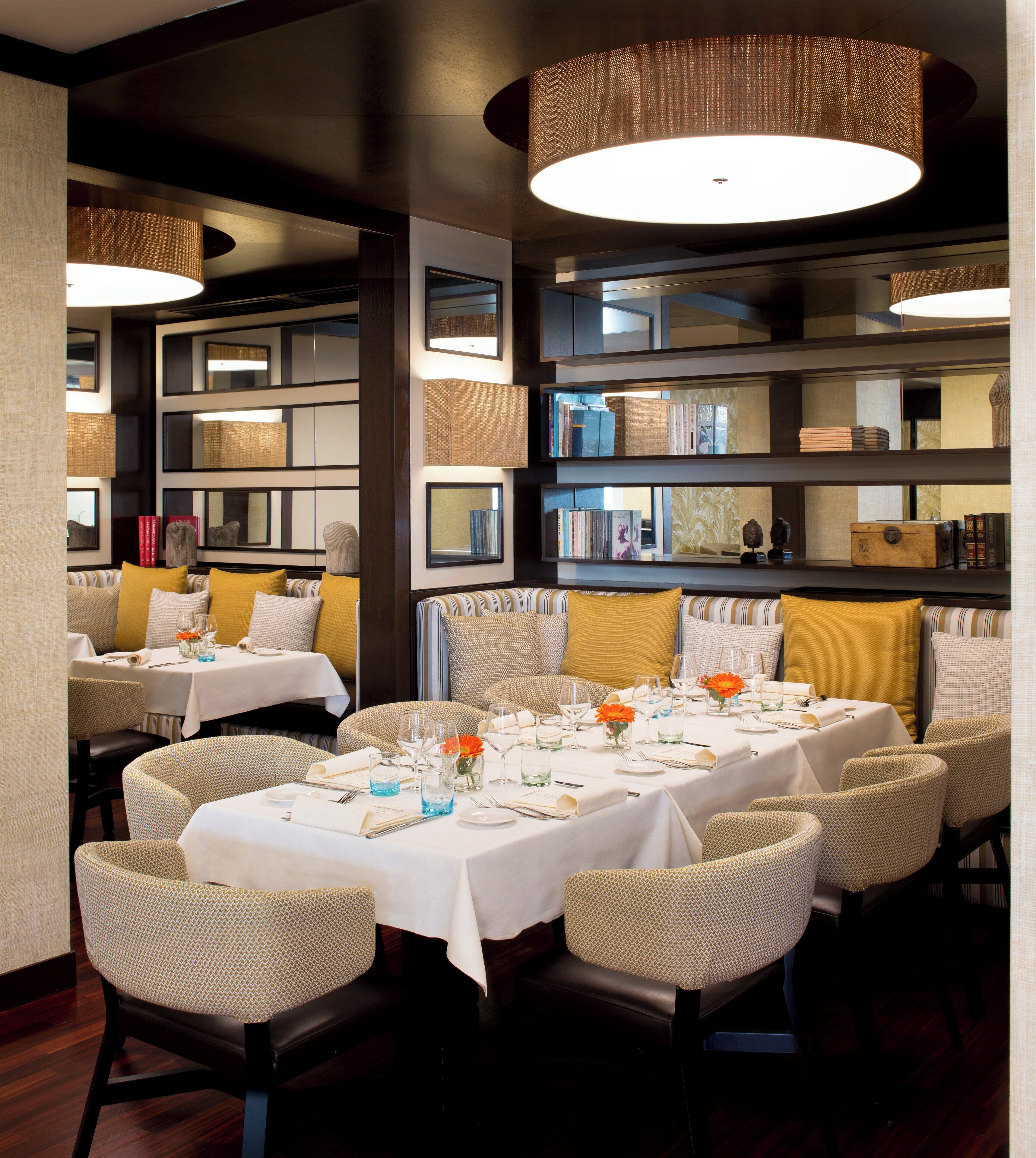 A restaurant with multiple tables set for dining, featuring wicker chairs and a variety of table settings.