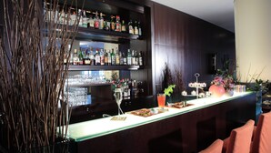 Zona de bar con estantes llenos de botellas de licor, mostrador y asientos.