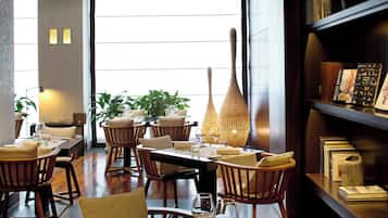 A restaurant with wooden furniture, a large vase, and a bookshelf with books.