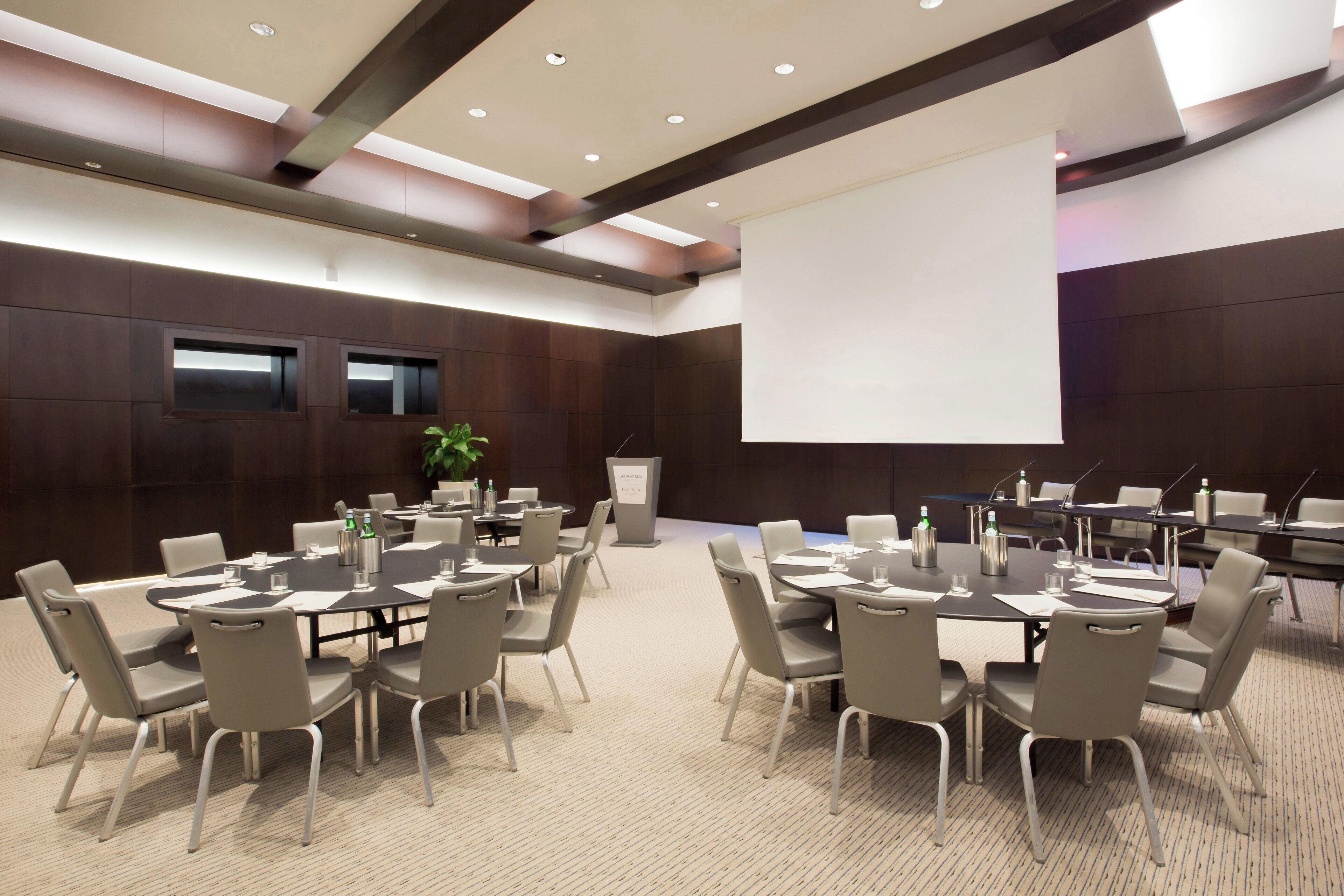 A conference room with multiple tables and chairs, a projector screen, and a podium.