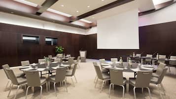 A conference room with multiple tables and chairs, a projector screen, and a podium.