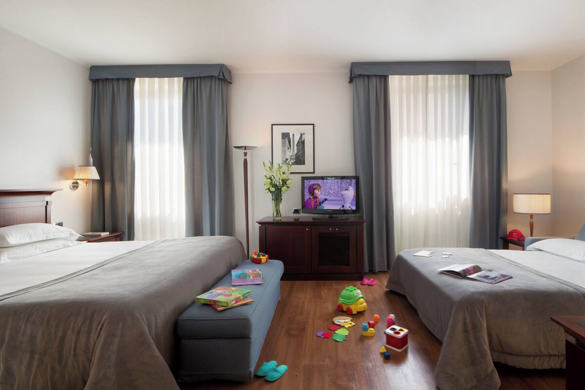 A hotel room with two beds, a TV, a desk with a lamp, and toys on the floor.