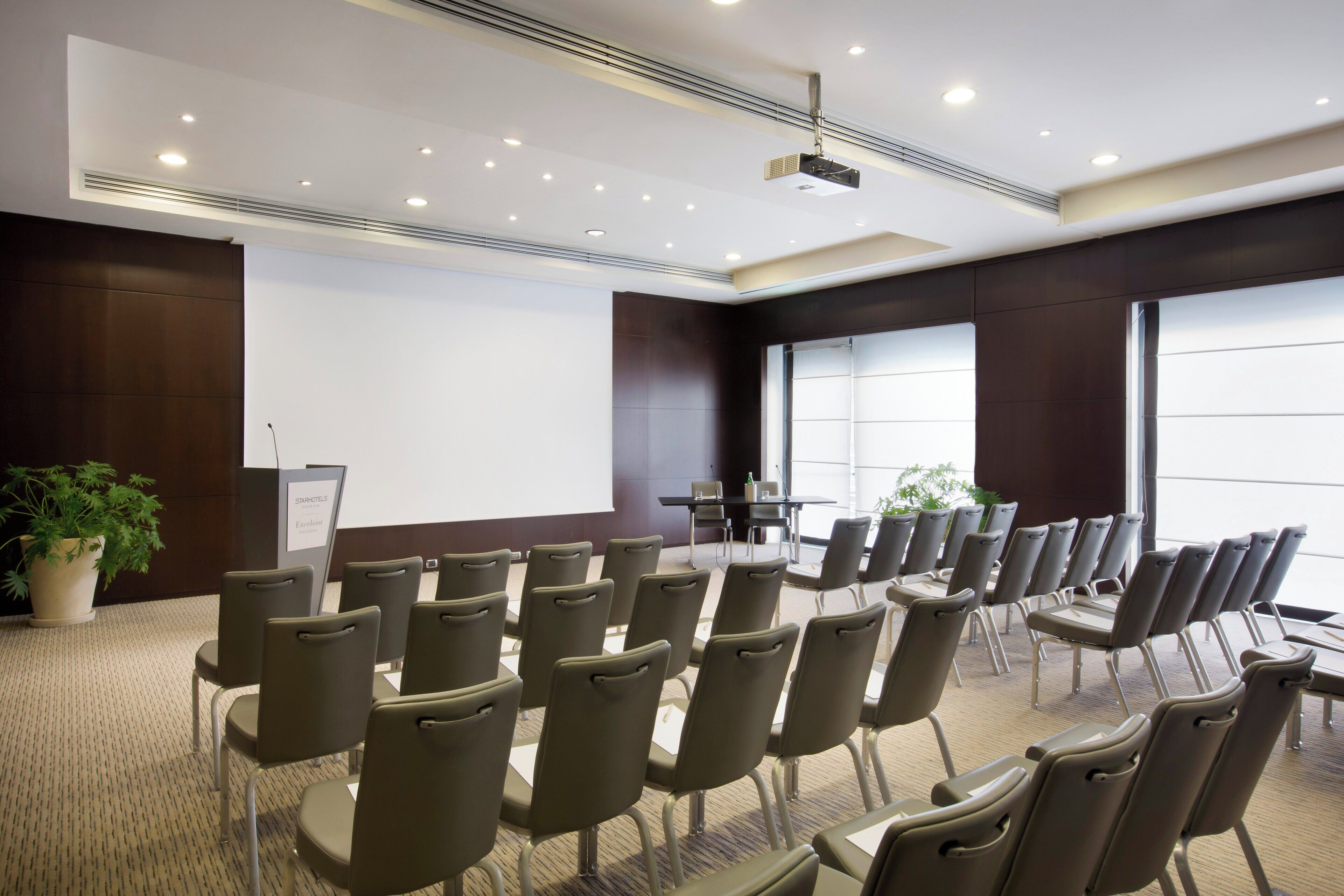 A conference room with rows of chairs, a projector screen, and a podium.