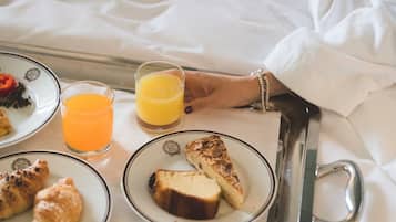 Una bandeja con alimentos para el desayuno, incluyendo cruasanes y tostadas, un vaso de jugo de naranja y una taza de café sobre una cama.