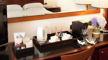 A hotel room with a bed, a bedside table with a tray containing a coffee maker, cups, and snacks, and a mirror above the bed.