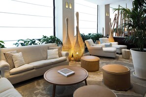 A modern lounge area with a sofa, ottomans, and a coffee table. - Starhotels Excelsior (Bologna)