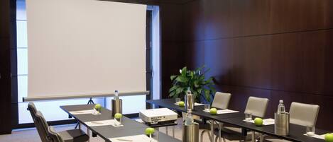 A conference room with a long table, chairs, a projector, and a screen.