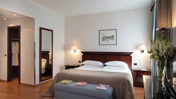 Une chambre d’hôtel avec un lit, des lampes de chevet, une table de chevet, un miroir, une commode, un vase avec des fleurs et un tableau encadré au mur.