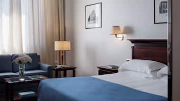 Habitación de hotel con una cama, un sofá, una mesita de noche, una lámpara y un cuadro en la pared.