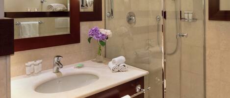 A hotel bathroom with a glass-enclosed shower, a sink with toiletries, and a mirror with a wooden frame.