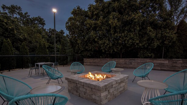 An outdoor patio with a stone fire pit, turquoise chairs, and a table. - Spark by Hilton Roanoke Civic Center (Roanoke)