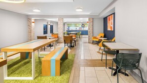 A modern dining area with multiple tables and chairs, a kitchen in the background, and a green carpet. - Spark by Hilton Roanoke Civic Center (Roanoke)
