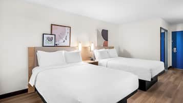 Habitación de hotel con dos camas individuales, cabecero de madera, mesitas de noche con lámparas y obras de arte en las paredes.