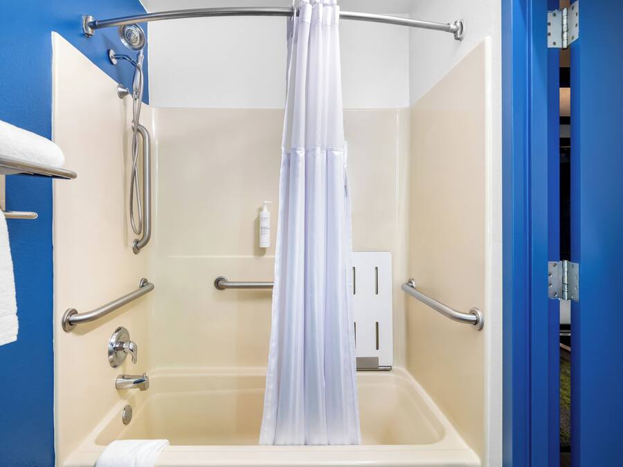 A bathroom with a bathtub, grab bars, a shower curtain, and a towel rack.