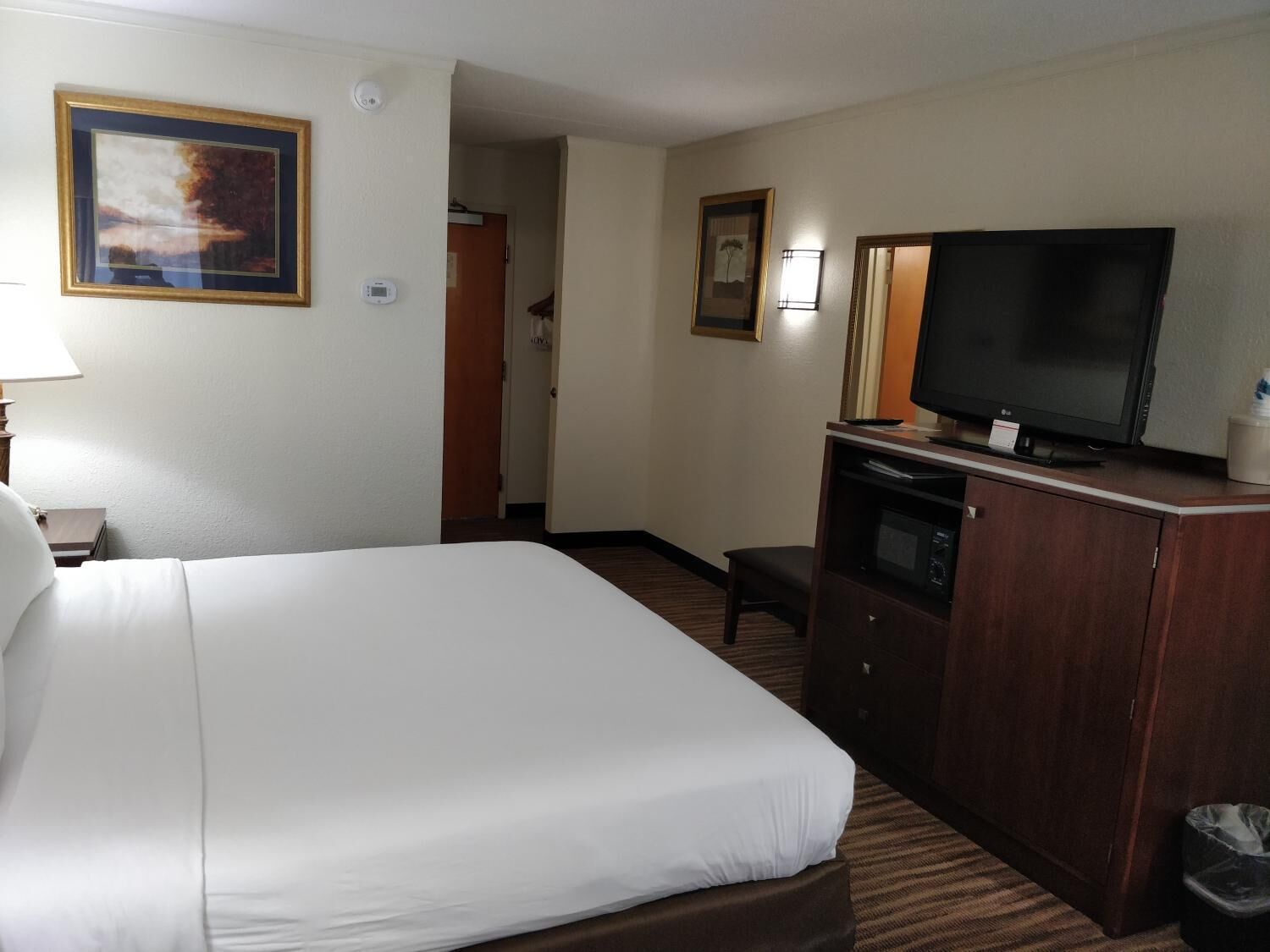 Habitación de hotel con una cama grande, un televisor sobre un mueble de madera y un cuadro en la pared.