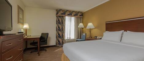 A hotel room with a large bed, a desk with a chair, a television, and two lamps.
