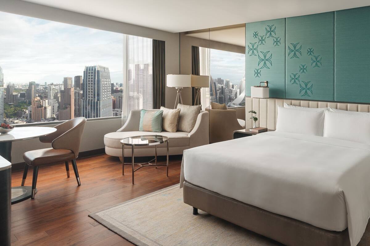 A modern hotel room with a large bed, a sofa, a desk, and a view of the city skyline.