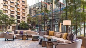 A modern lounge area with a sofa set, coffee table, and lamp, overlooking a cityscape with tall buildings and greenery. - InterContinental Bangkok by IHG (Bangkok)