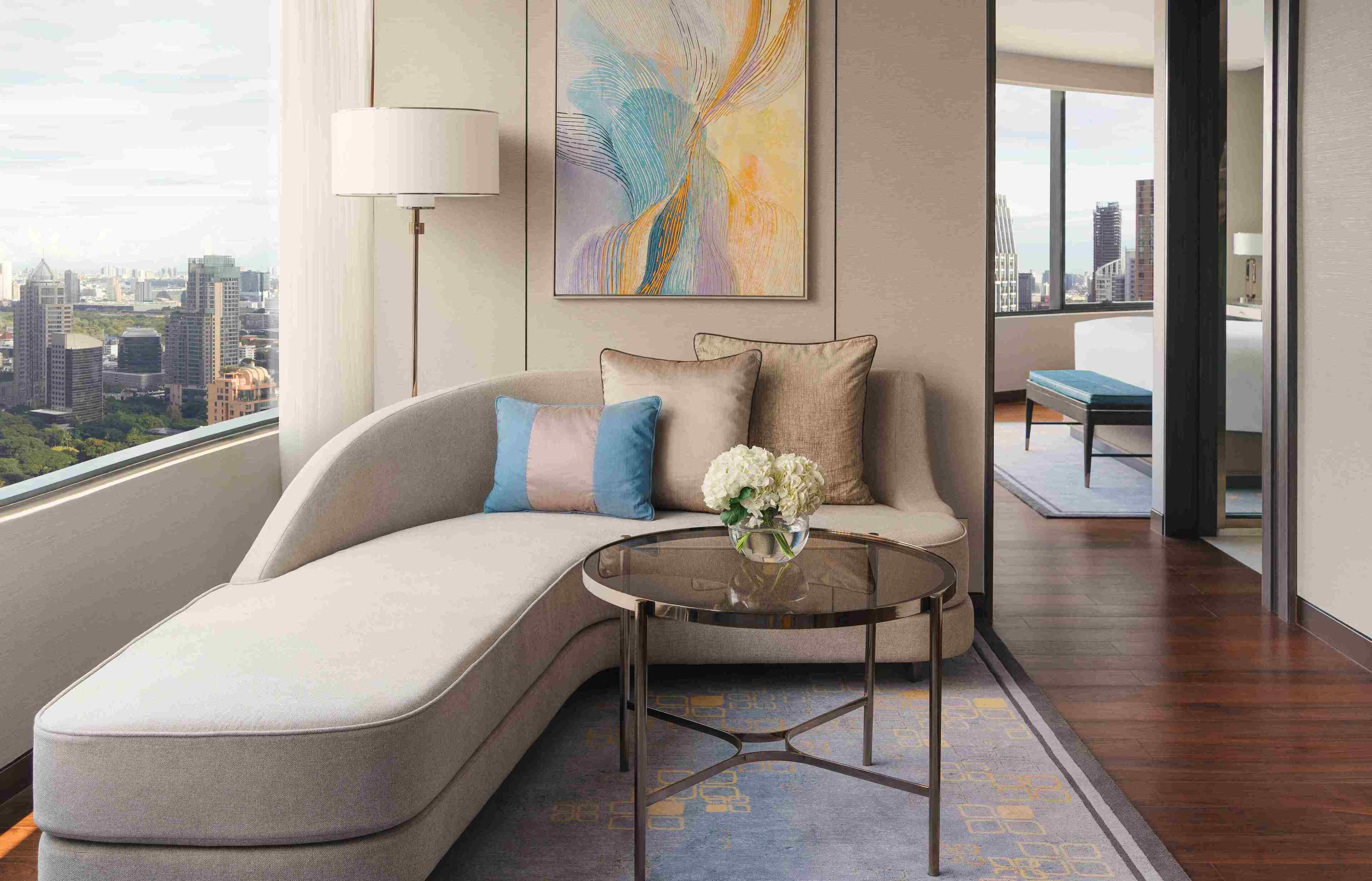 A modern living room with a curved sofa, a glass coffee table, and a large abstract painting.