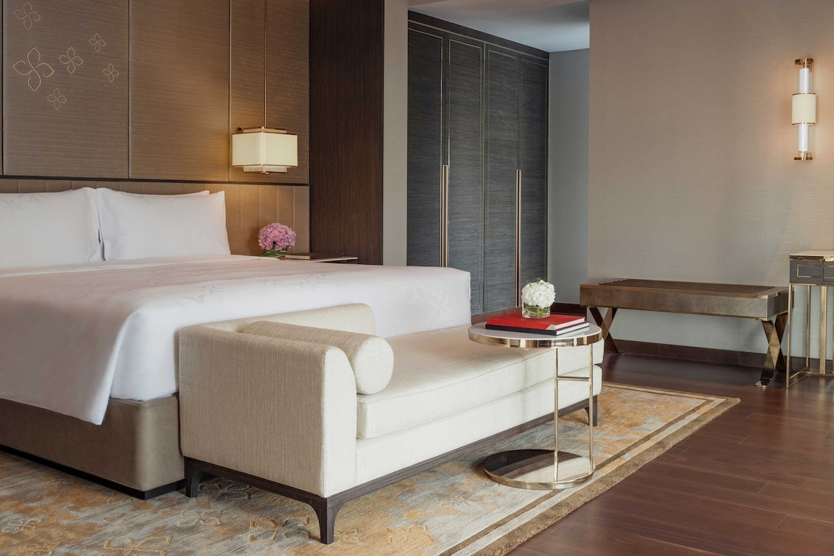 A modern hotel room with a large bed, a small sofa, a round side table, and a desk.