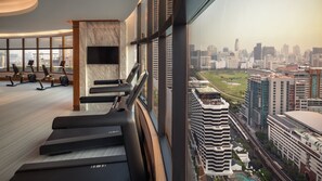 Un gimnasio con cintas de correr y equipo de ejercicio, amplias ventanas con vistas a la ciudad y un diseño interior moderno.