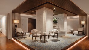 Un moderno vestíbulo de hotel con una zona de estar central, detalles de madera y una alfombra estampada.