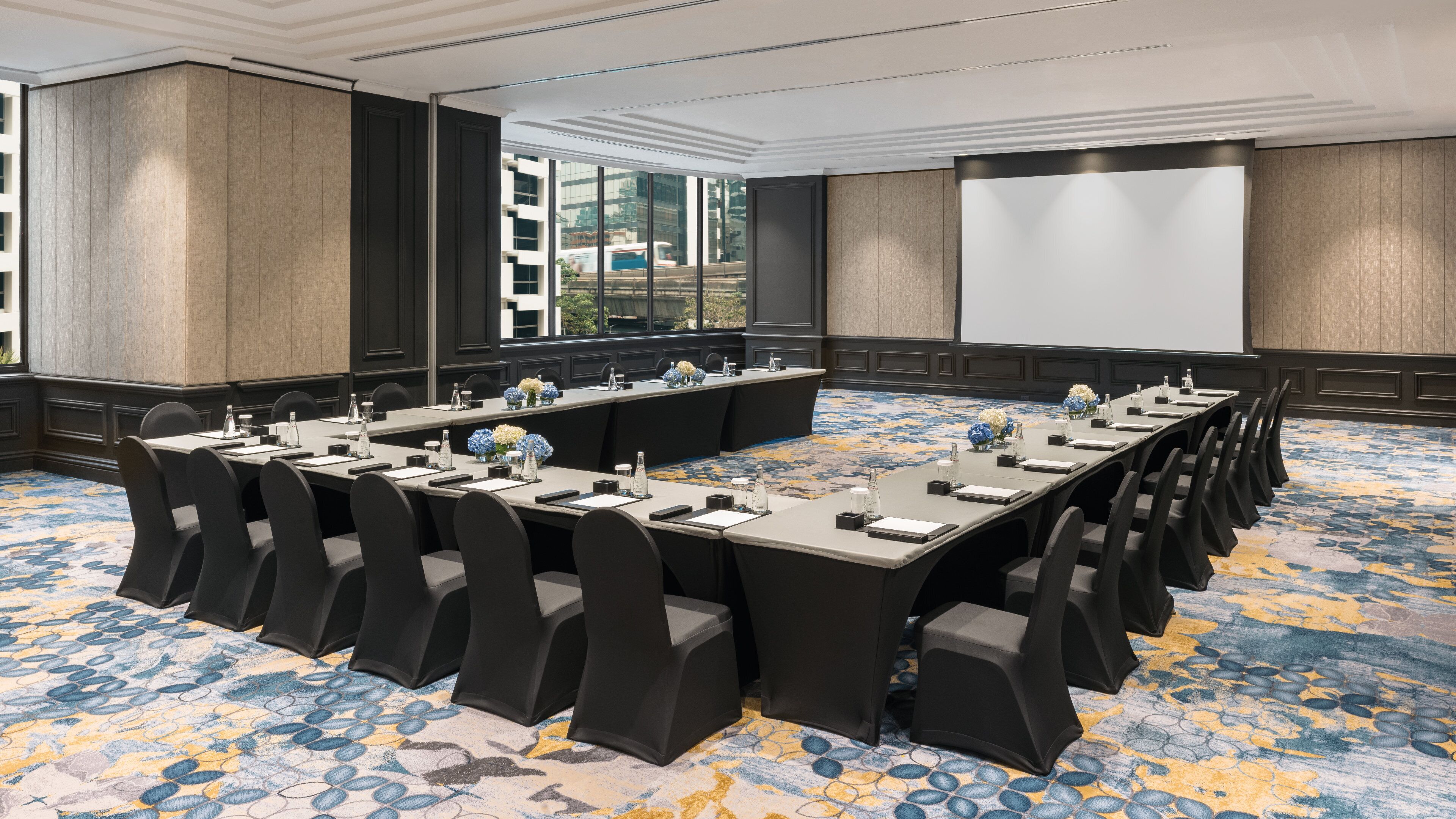 A conference room with a long table, chairs, and a projector screen.