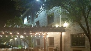 An outdoor seating area with wicker furniture, a central fire pit, and string lights.