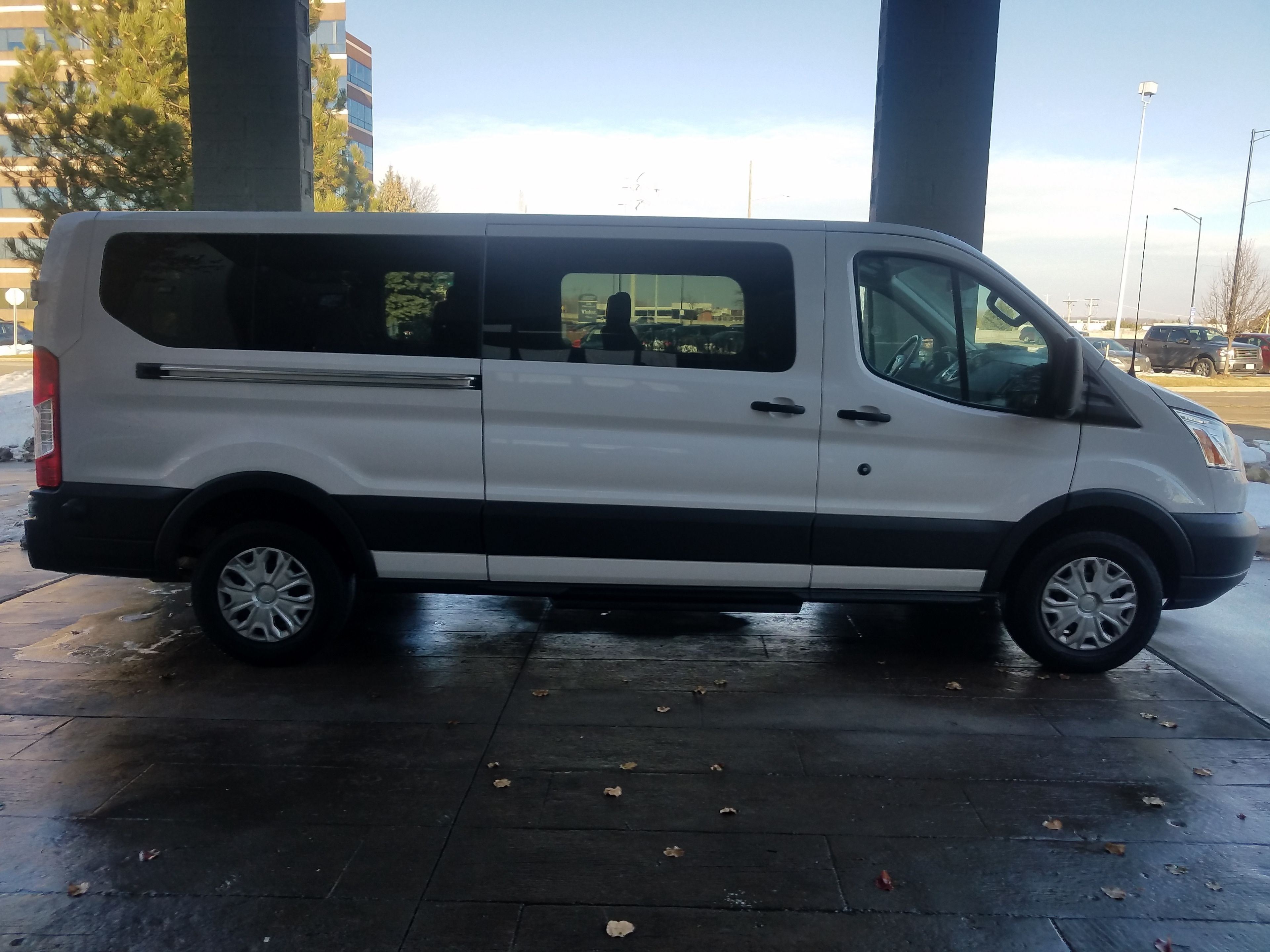 A white van parked under a bridge with a clear view of the sky and buildings in the background.