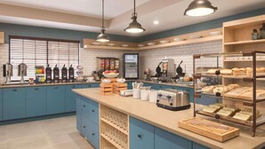 A kitchen with blue cabinets, a central island with a coffee machine, a refrigerator, and a glass display case with pastries.