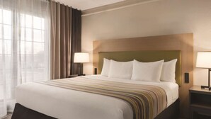 A hotel room with a large bed, two bedside lamps, a headboard, and a window with curtains.
