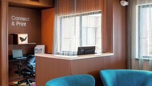 Un espace d’accueil d’hôtel comprenant un comptoir, deux fauteuils bleus, une moquette colorée et un panneau indiquant « Connexion et impression ».