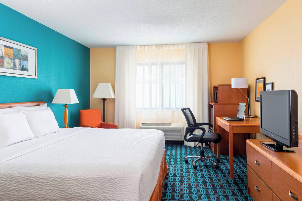 A hotel room with a bed, desk, chair, TV, and a window with curtains.