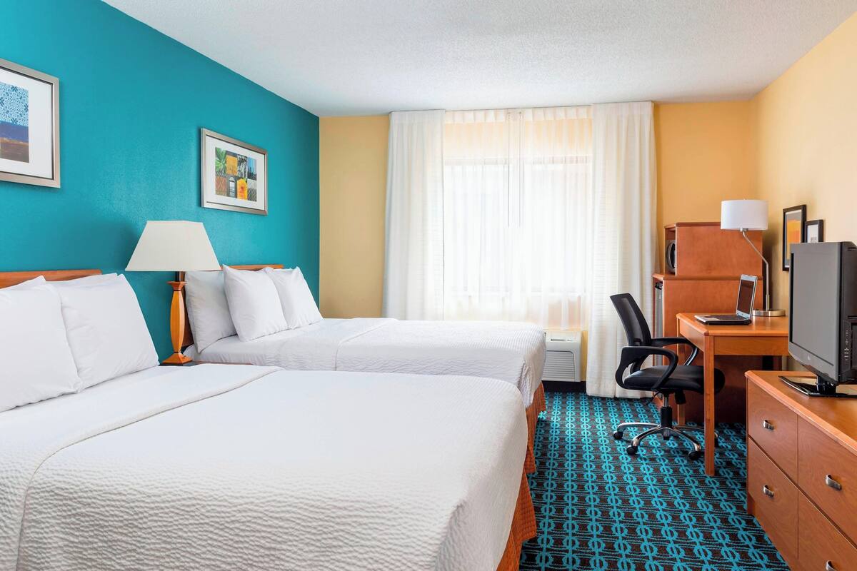 A hotel room with two beds, a desk with a computer, a TV, and a chair.